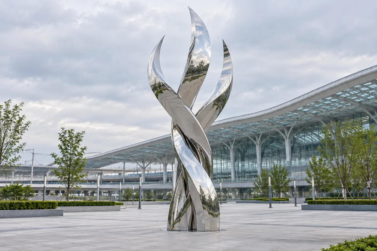 Mirror-polished stainless steel ribbon sculpture in front of a rail transit terminus